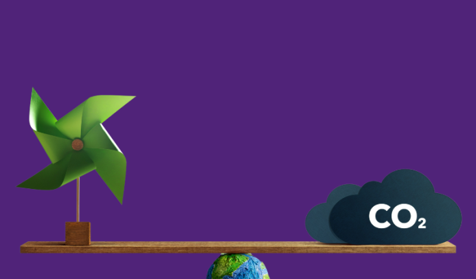 A green windmill on the left and a dark cloud labeled “CO₂” on the right are balanced on a wooden plank. The plank is supported by a small Earth globe at the center, symbolizing the balance between renewable energy and carbon emissions. The background is solid purple.